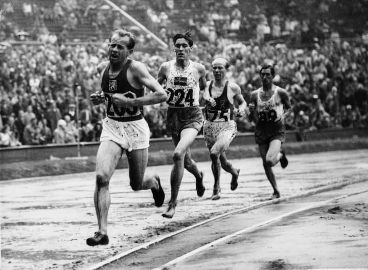 Emil Zátopek leads a pack of runners on a rain-soaked track during the 5000m final at the 1952 Helsinki Olympics, moments before claiming gold.