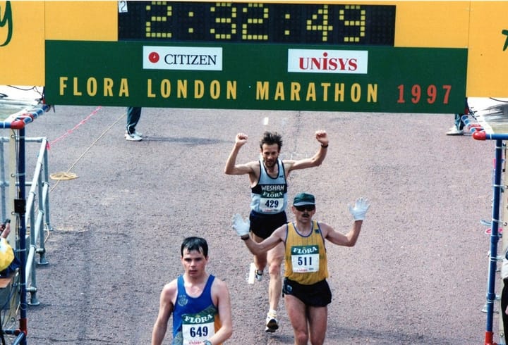 Pete Johnson finishing the 1997 Flora London Marathon in 2:32:49, raising his arms as he crosses the line behind two other runners.