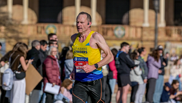 Runner in St Albans Striders vest racing mid-marathon at Seville, focused and working hard, with spectators blurred behind during a fast, flat city-centre section.