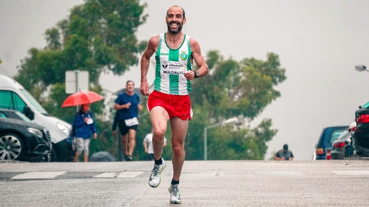 Male runner racing uphill on wet road in light rain during a road race, with other runners and spectators in background